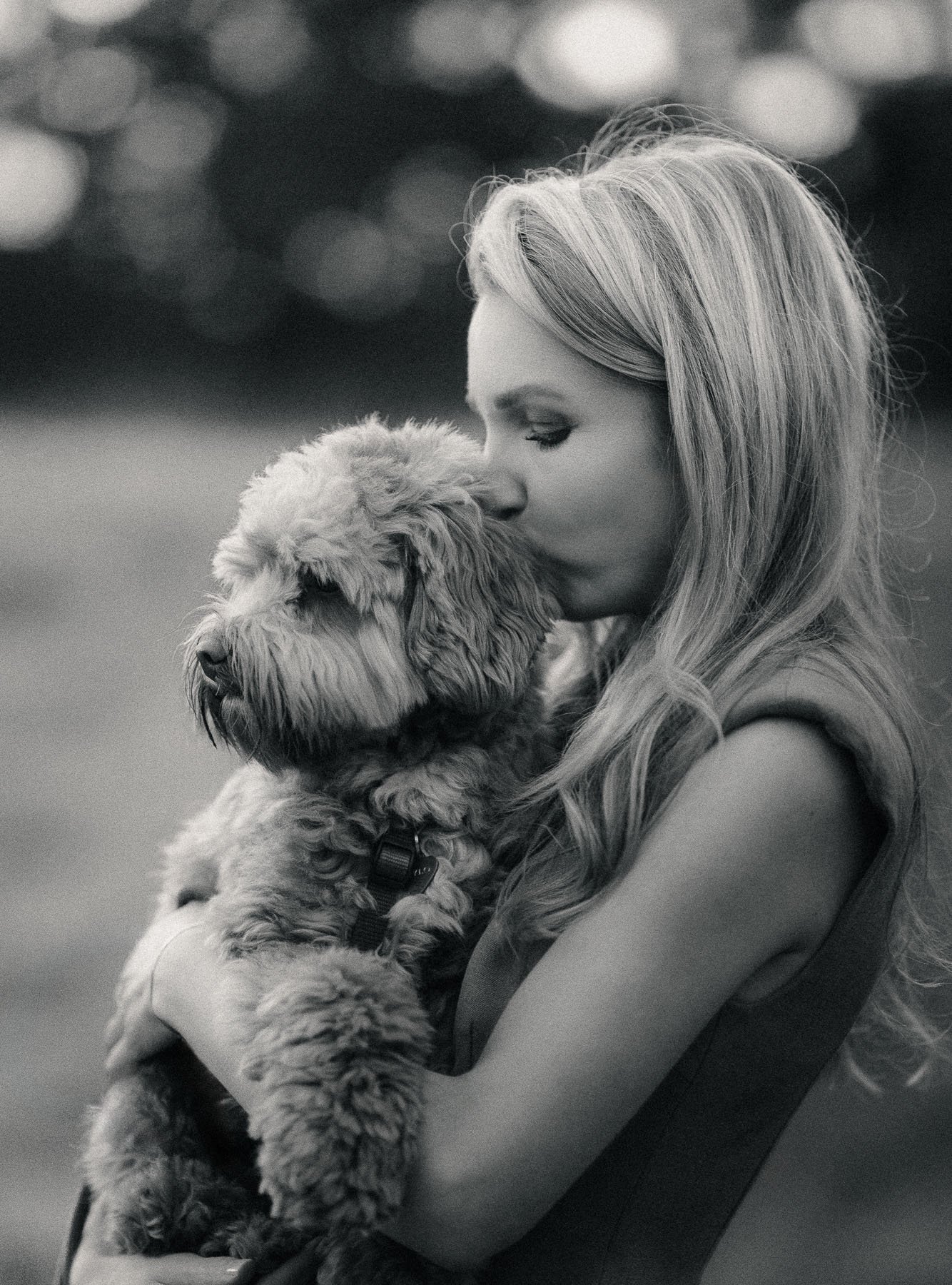 A woman with long, wavy hair holds a fluffy puppy close to her face.