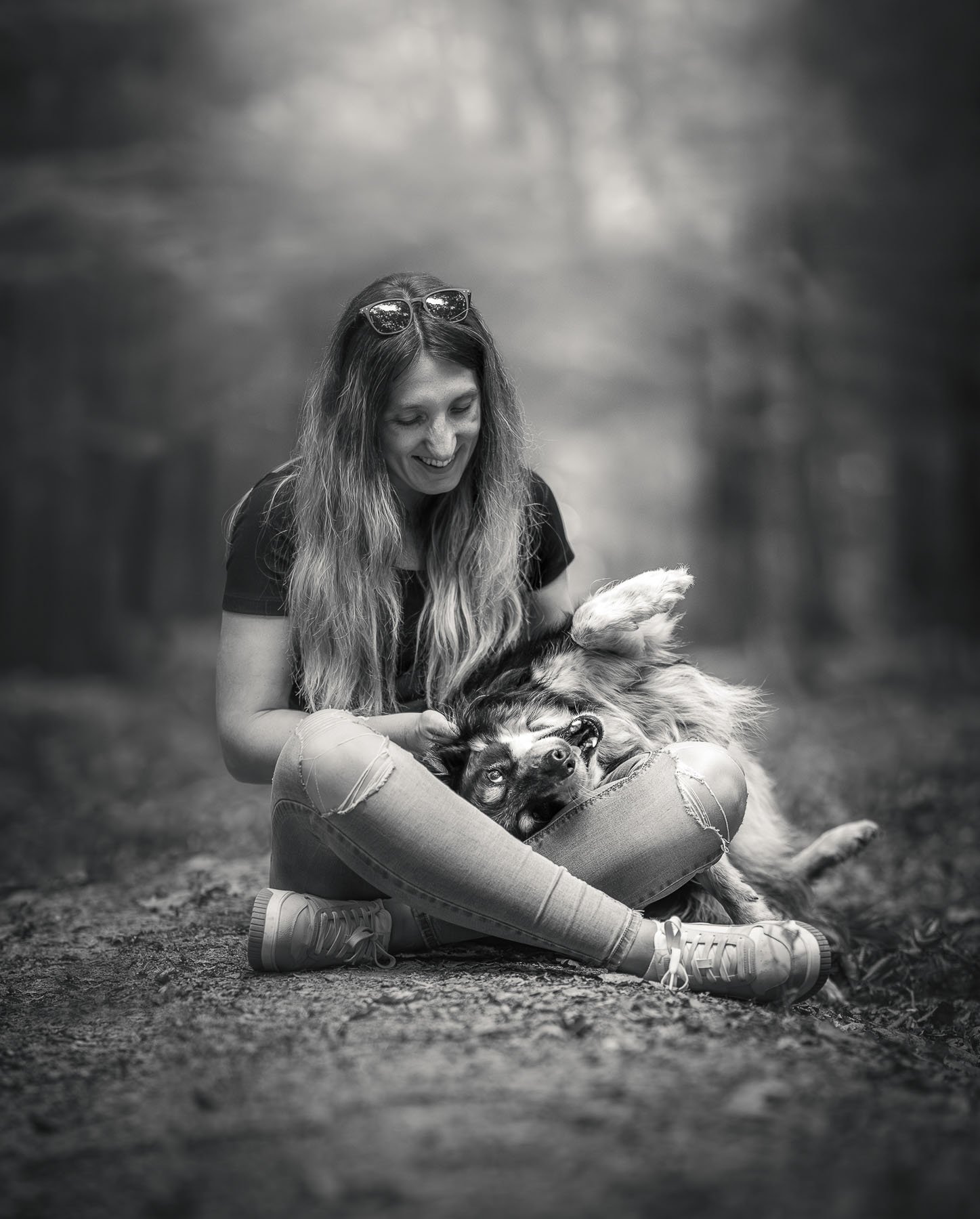 A smiling woman wearing sunglasses hugs her dog.