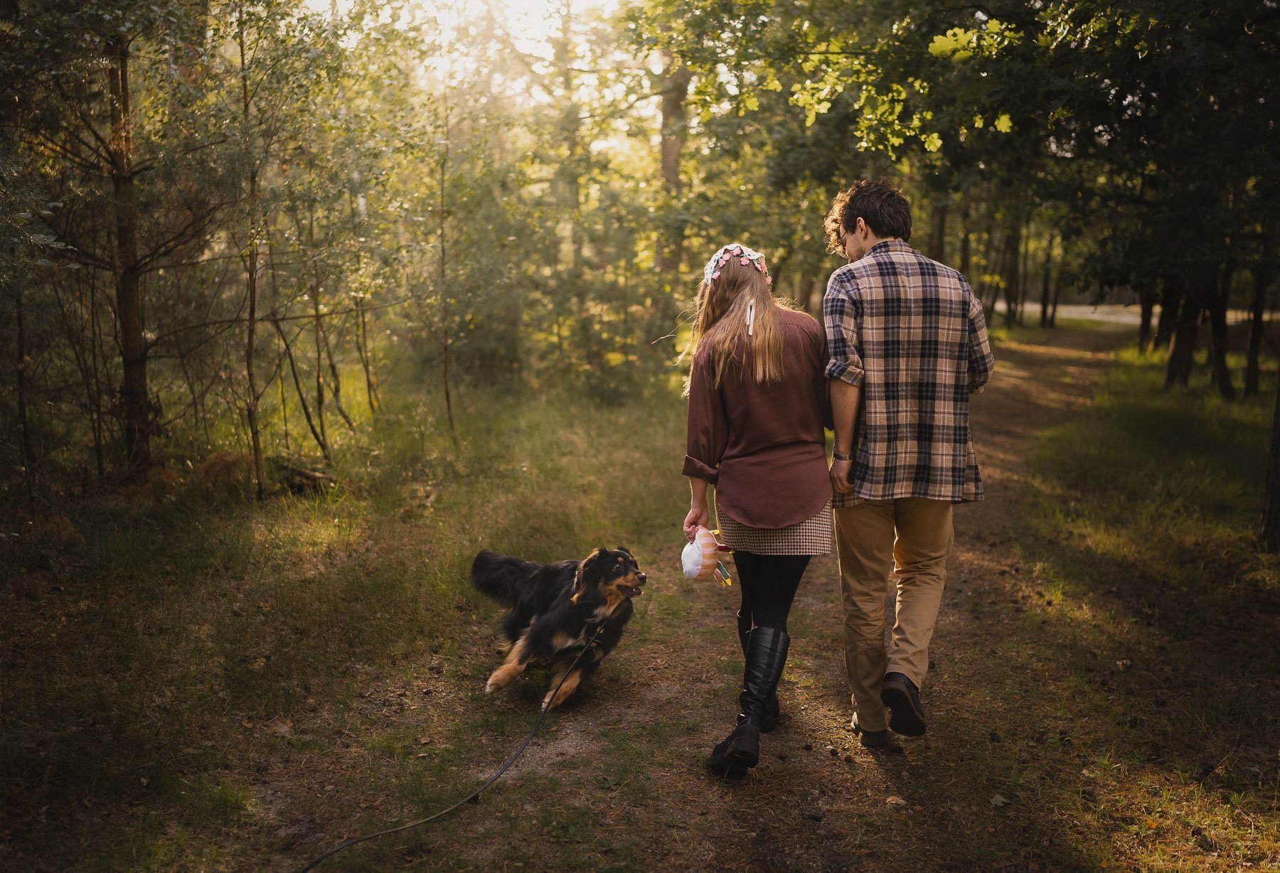 A couple walks with their dog through a forest.