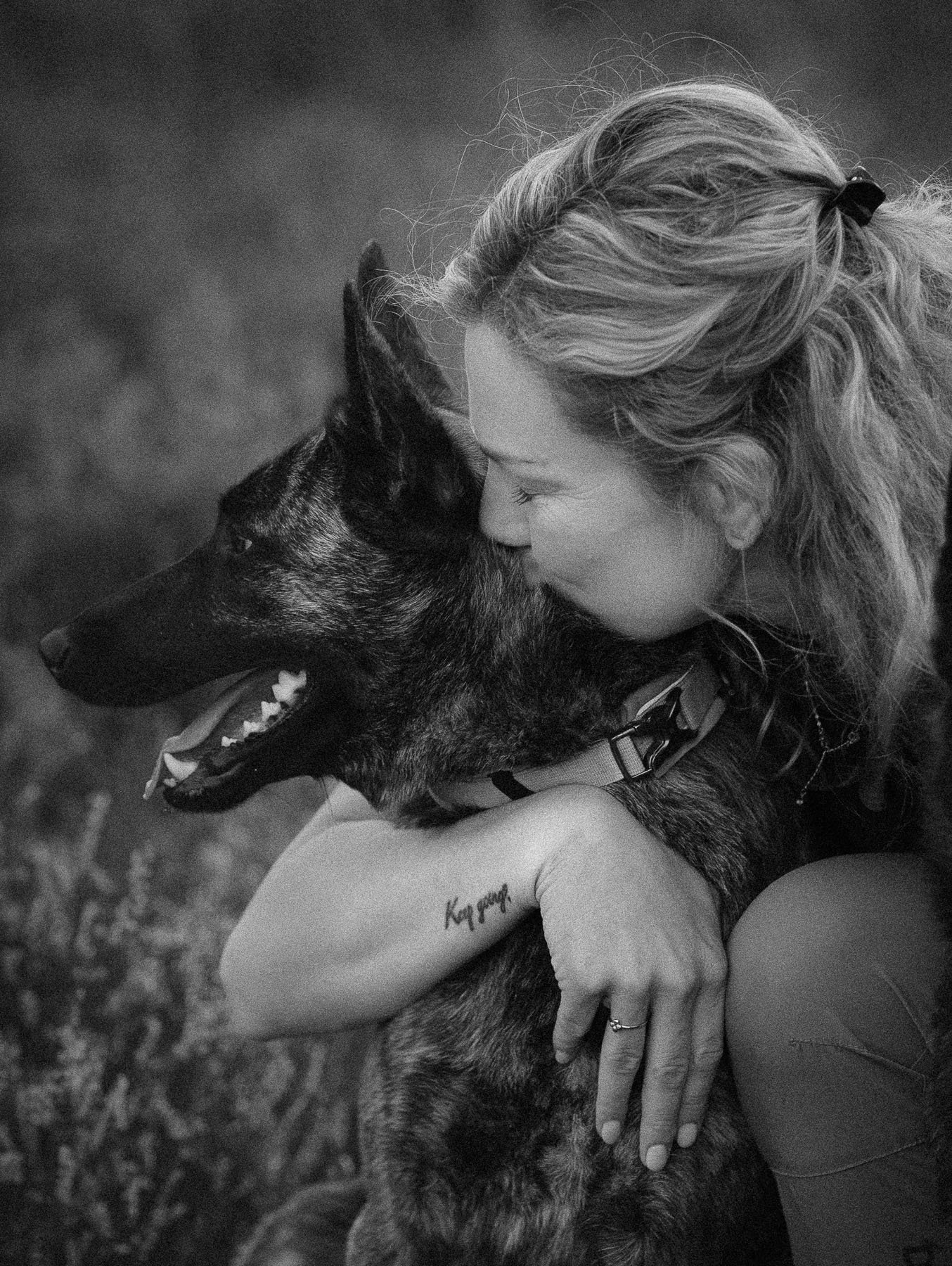 Black-and-white photo of a woman hugging and kissing her dog.
