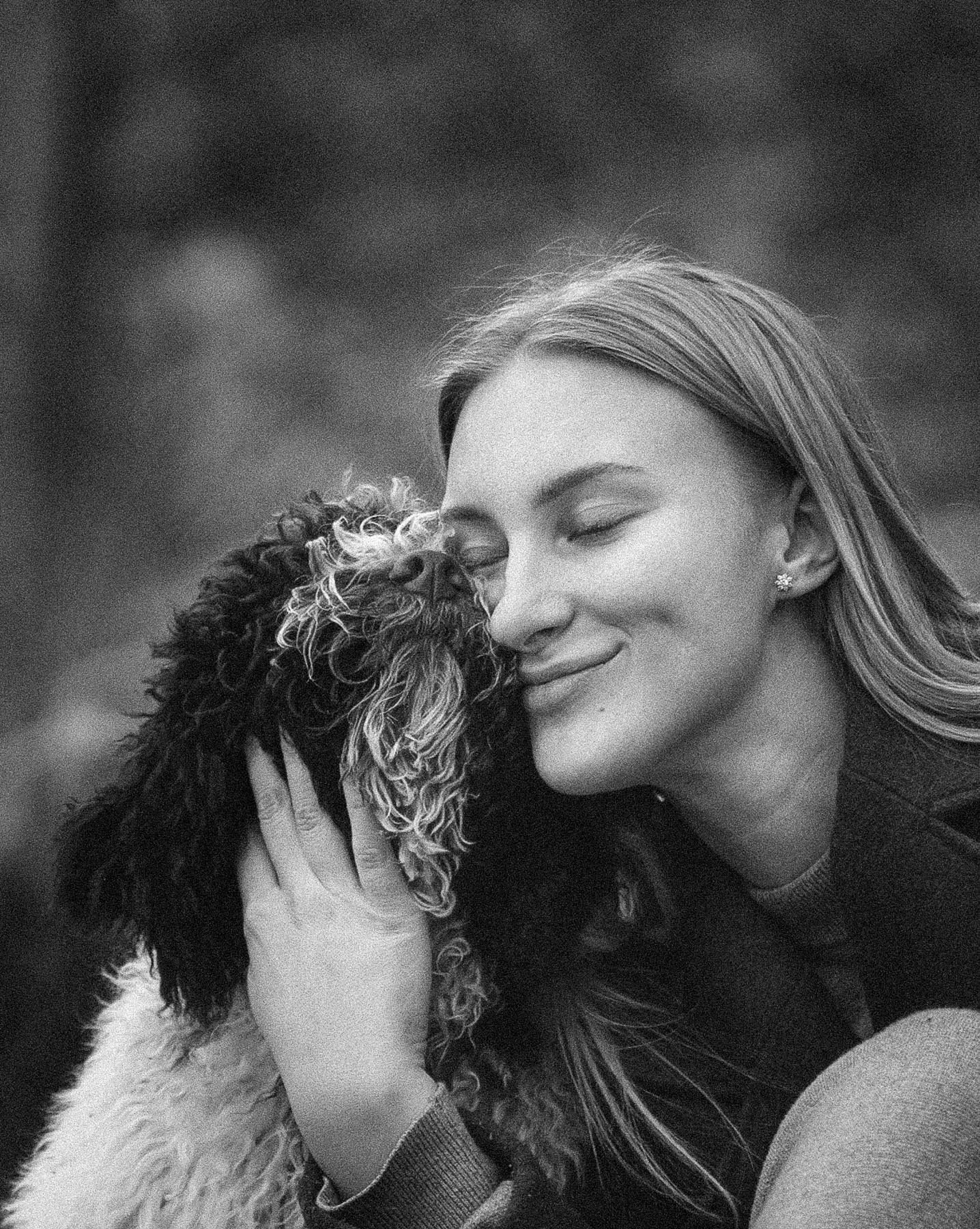 Black-and-white photo of a woman with her eyes closed, hugging her labradoodle.
